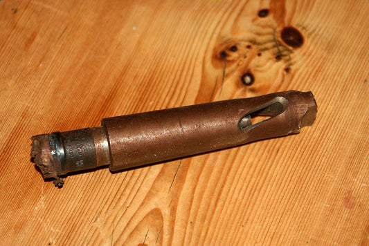 A worn drill bit attachment lying on a wooden surface